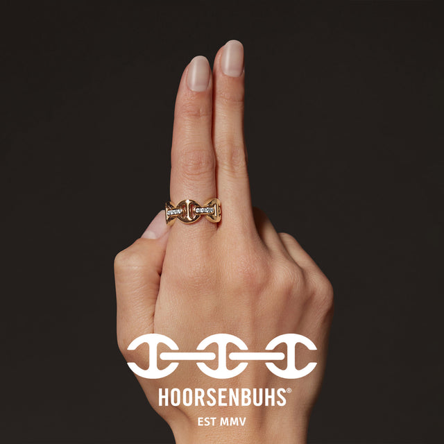 Hand wearing a gold ring with 'Hoorsenbuhs' logo in the foreground 