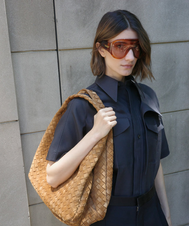 Woman holding a Bottega Veneta Intrecciato hobo bag wearing a navy blue shirtdress 