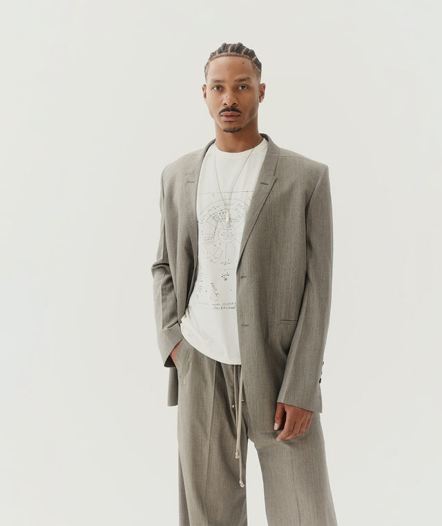 Man wearing a gray jacket and wide leg pants with a white graphic print tee-shirt, all by Rick Owens 