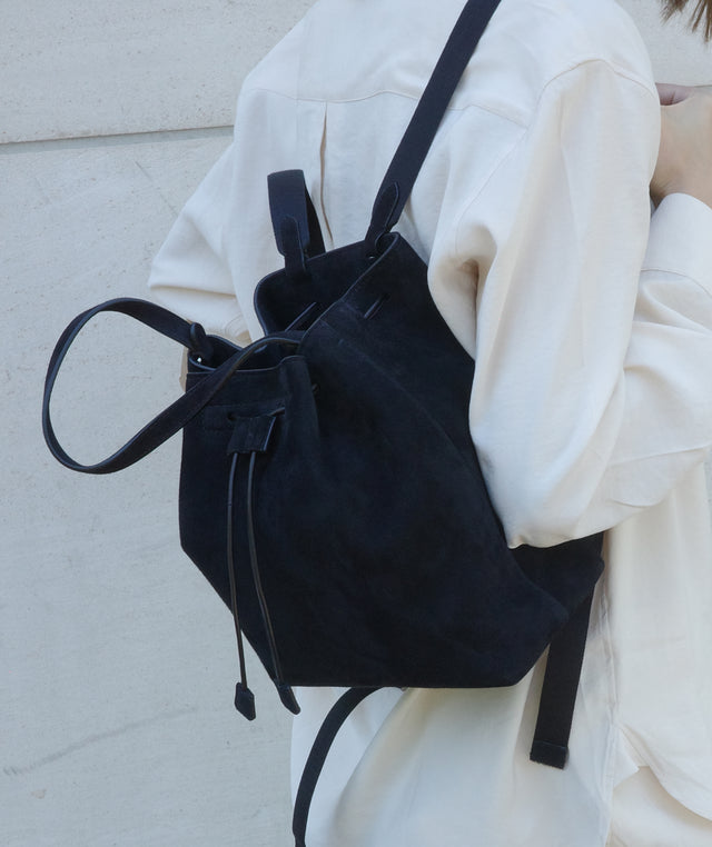 Black suede backpack by The Row worn over one shoulder against a light background 