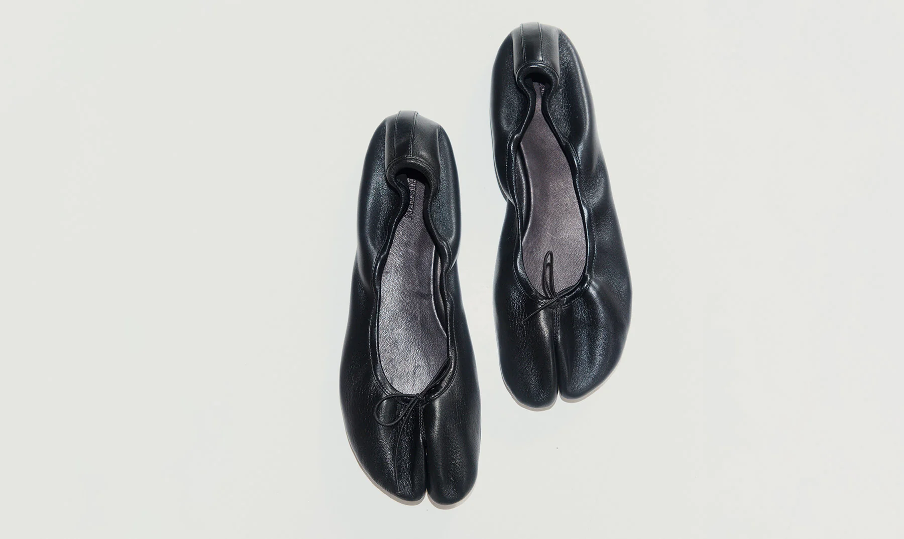 A pair of black leather tabi-style ballet flats by Christen with a split toe design, shown from a top-down view on a light gray background.