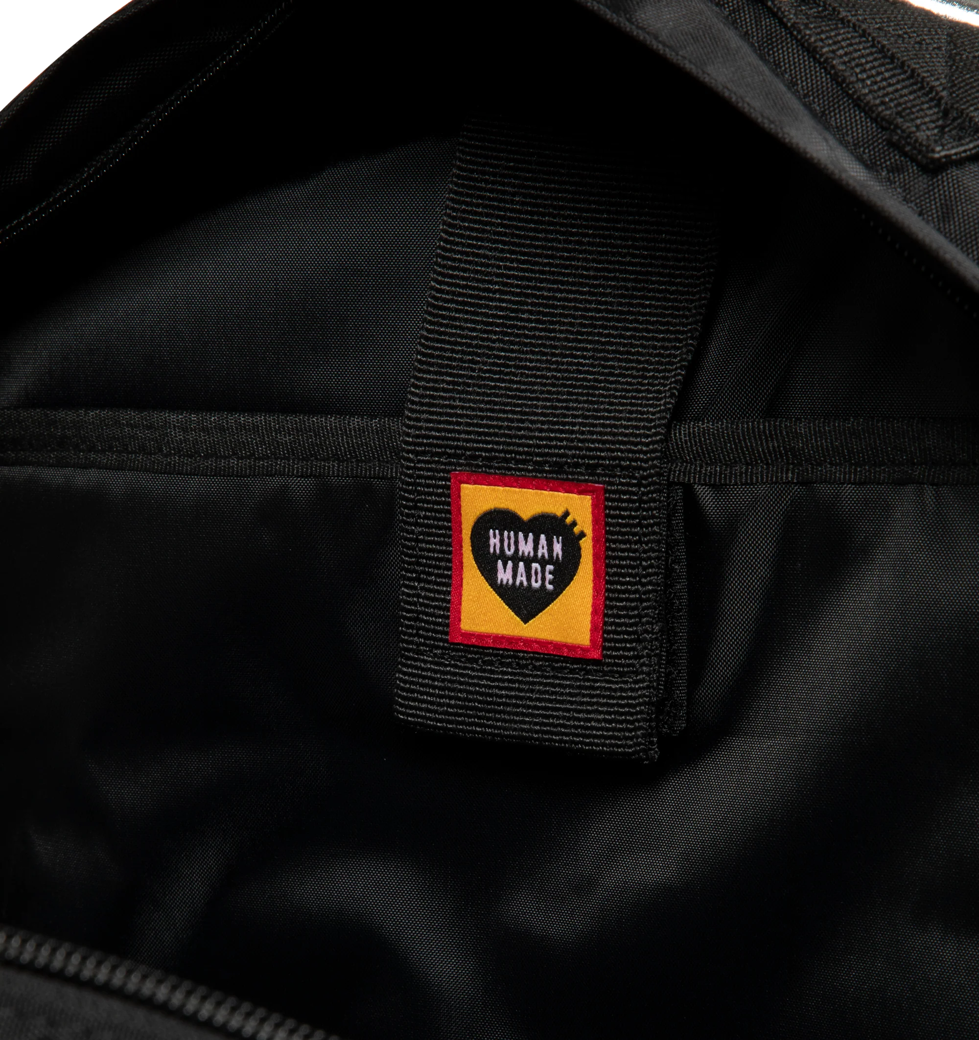 Image 3 of 3 - BLACK - Human Made Military Backpack is crafted from lightweight nylon Oxford fabric and features a military-inspired silhouette with stencil-style graphics and modular attachment functionality. Designed with a front flap pocket with buckle strap closure, a cushioned sleeve for a laptop or tablet, mesh-padded back panel, adjustable waist belt, and B4-sized storage capacity for everyday versatility. Main Material: Shell: 100% Nylon. Lining: 100% Polyester. Dimensions: 44 cm H x 32 cm W x 11 cm