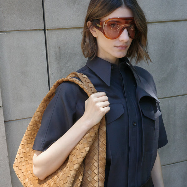 Woman wearing sunglasses and holding a woven bag by Bottega Veneta