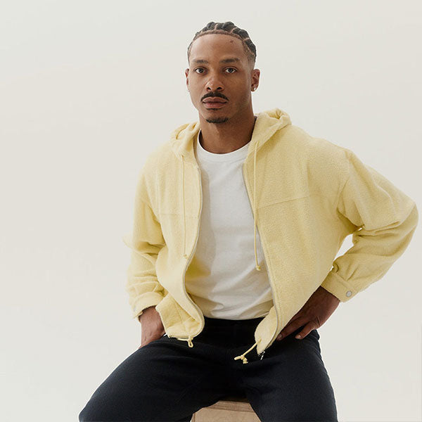 Man wearing a light yellow hoodie over a white shirt by Auralee