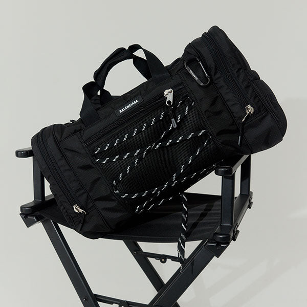 Black Balenciaga bag with white stitching on a black chair against a light gray background