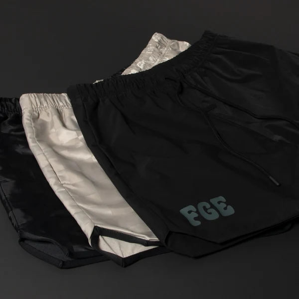Three pairs of athletic shorts in black and metallic silver by Fear of God with 'FGE' logo on the left leg.