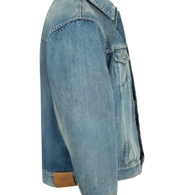 Image 3 of 3 - BLUE - SAINT LAURENT Loose Trucker Jacket featuring loose-fit, certified cotton, a pointed collar, front buttons, flap pockets, cotton lining, two patch pockets with buttoned flap at the chest, two welt pockets at the front, one-button cuffs and logo embossed leather jacron. 100% cotton. Made in Japan. 