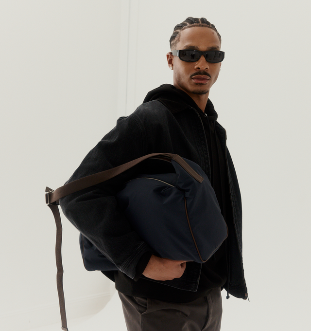 Image 2 of 5 - NAVY - THE ROW E/W Logan Bag featuring contoured shoulder bag in crisp technical nylon with turned-edge construction, woven adjustable flat strap, leather piping, and top zipper closure. 15.75 x 10.63 x 7.48 in. 45% cotton, 25% nylon, 30% calfskin leather. Lined in 56% cotton, 44% nylon. Made in Italy.